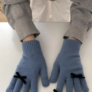 Close-up of blue knitted gloves with black bow accents on a minimalist white surface