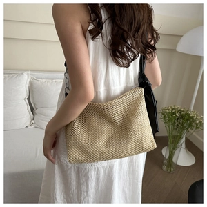 Detail of hand-woven straw tote bag with black leather shoulder strap and mesh texture