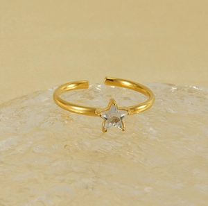 Detail of adjustable gold star ring with white zircon on textured glass surface