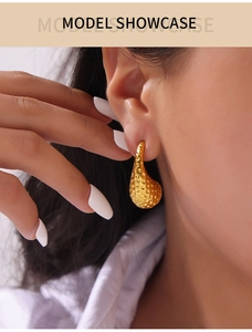Gros plan détaillé de boucles d'oreilles goutte dorées avec texture martelée sur modèle