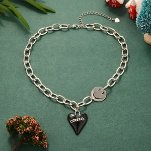 Detail of silver link chain necklace with black heart and smiley face charms on green background