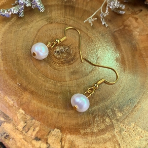 Elegant natural freshwater pearl drop earrings with gold hooks on a rustic wood base