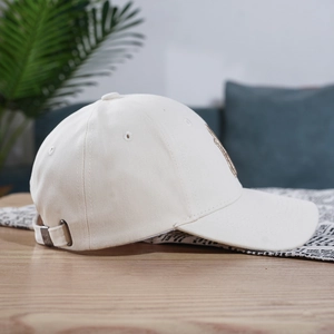 Detail view of white cotton baseball cap showing golden embroidery and metal buckle