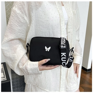 Detail of black nylon crossbody bag featuring silver butterfly and letter strap
