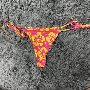 Detail der pinkfarbenen Bikini-Hose mit tropischem Blumenmuster und Seitenbändern