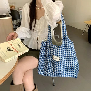 Blue and white checkered knitted tote bag with wide straps shown in a cozy cafe setting