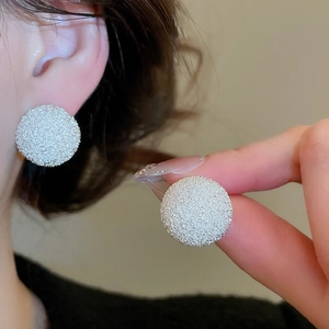 Detail of silver round stud earrings with matte frosted texture on a model ear