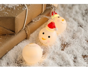 Close-up of snowman LED fairy lights with red hats emitting warm yellow glow in snow