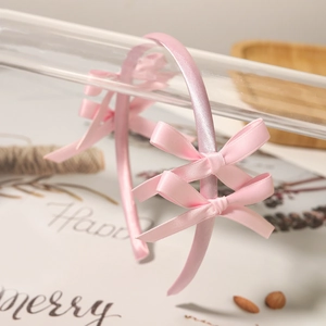 Close-up of pink satin headband featuring three delicate bows in ballet aesthetic style