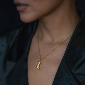Close-up of 18K gold stainless steel cowboy boot pendant necklace worn by a model