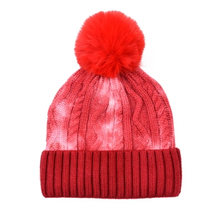Detail of red tie-dye knit hat with large faux fur pompom and thick cable pattern