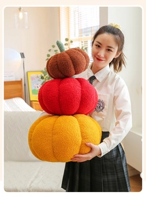 Close-up of three stacked plush pumpkin pillows in brown, red, and orange soft fabric