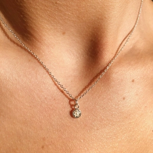 Close-up of a delicate silver necklace with a round sparkling zircon pendant worn by a model