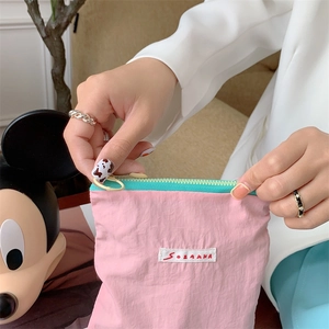 Detail showing hand holding a pink wrinkled nylon pouch with a cyan zipper and yellow puller
