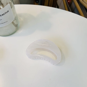 Minimalist semi-circular cream hair claw clip with smooth acrylic finish on white desk