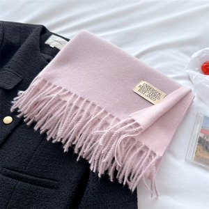 Detail of pink cashmere-like scarf featuring fringe and a gold rectangular metal tag