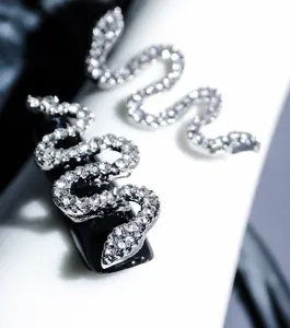 Macro shot of silver S-shaped snake nail art charm with micro-set zircons on black nail