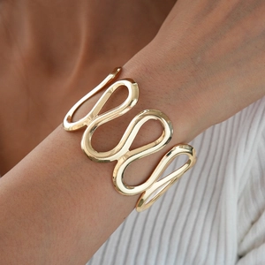 Polished gold wave bangle featuring a sleek S-curve design on a model's wrist