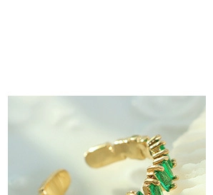 Detail of gold ear cuff with green rectangular gemstone on a textured shell