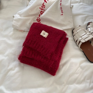 Detail of red wool knit scarf with minimalist brand tag on a cozy white background