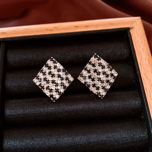 Macro detail of geometric checkered diamond earrings inside a black velvet jewelry box