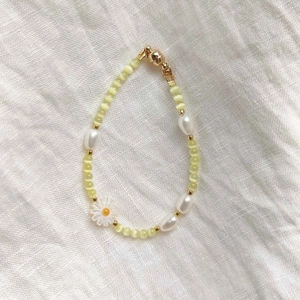 Detail view of yellow cat eye beads and white daisy charm on a gold-plated clasp necklace
