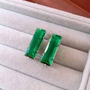 Close-up of rectangle green zircon earrings in silver claws on grey velvet background