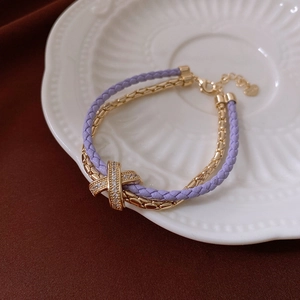 Detail of purple woven leather bracelet with gold chain and zircon X-shaped buckle