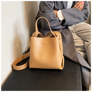 Detail view of khaki leather bucket bag with top handle and brand embossing on a table