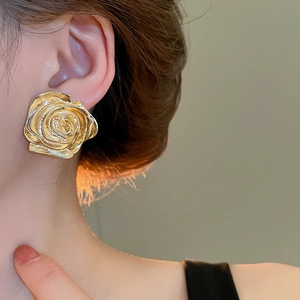 Dettaglio di grandi orecchini a rosa dorata con petali opachi indossati sul lobo dell'orecchio