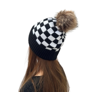 Women's black and white checkered knit beanie with a brown faux fur pom-pom on top