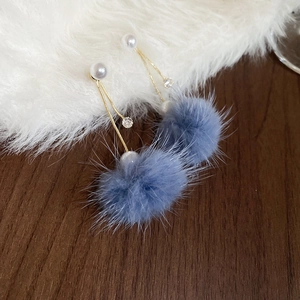 Detail of drop earrings with grey pom-poms, white pearls, and gold-plated chains