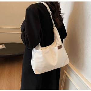 Side view of a white high-capacity canvas hobo bag worn by a model in a minimalist room