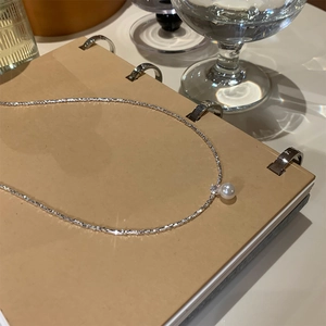 Detail of silver pearl necklace with zircons resting on a leather notebook