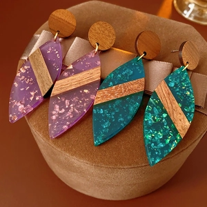 Détail de boucles d'oreilles en forme de feuille en bois et résine avec feuilles d'or