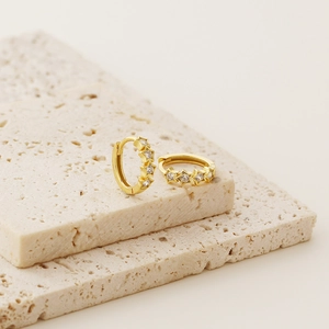 Macro detail of gold star earrings with sparkling zircon inlay on beige stone blocks
