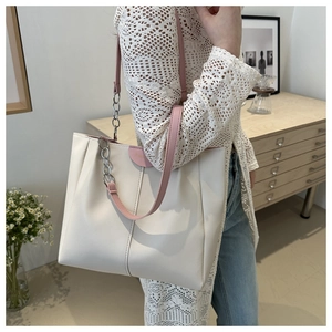 Dettaglio della borsa tote avorio con tracolla rosa e catena d'argento su un modello