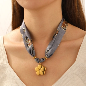 Close-up of a floral silk scarf necklace with a gold five-petal flower pendant on neck