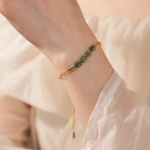 Détail d'un bracelet vintage doré avec pierres vertes carrées porté au poignet