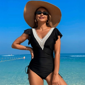 Deep V-neck black one-piece swimsuit with white lace trim and flutter sleeves at beach