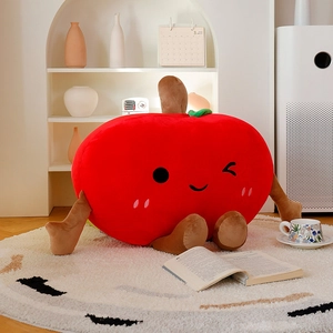 Cute red apple plush toy pillow with long limbs and winking face in cozy home setting