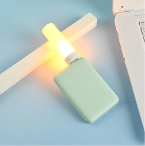 USB warm yellow LED flame night light plugged into a green power bank on blue surface