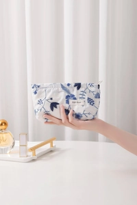 Détail de broderie florale sur une trousse de maquillage en lin blanc tenue à la main