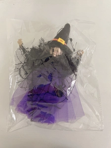 Detail of a purple and black Halloween witch doll with spider web lace in clear packaging