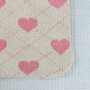 Detailed macro view of the beige knit tote bag fabric with pink heart pattern textures
