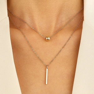 Close-up of double layer gold necklace with bead and vertical bar pendants on model
