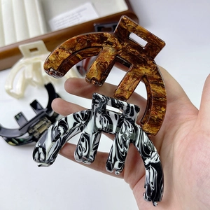 Detail showing amber and black-white marble acetate claw clips held in hand for scale