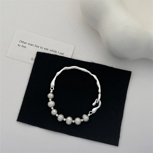 Detail of baroque freshwater pearl and irregular branch-style silver bracelet on dark background