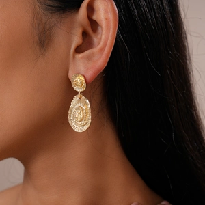 Gros plan de boucles d'oreilles dorées géométriques texturées portées par un mannequin