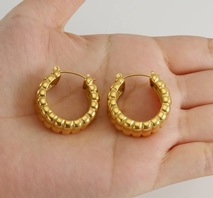 Close-up of golden U-shaped earrings with textured croissant surface on hands